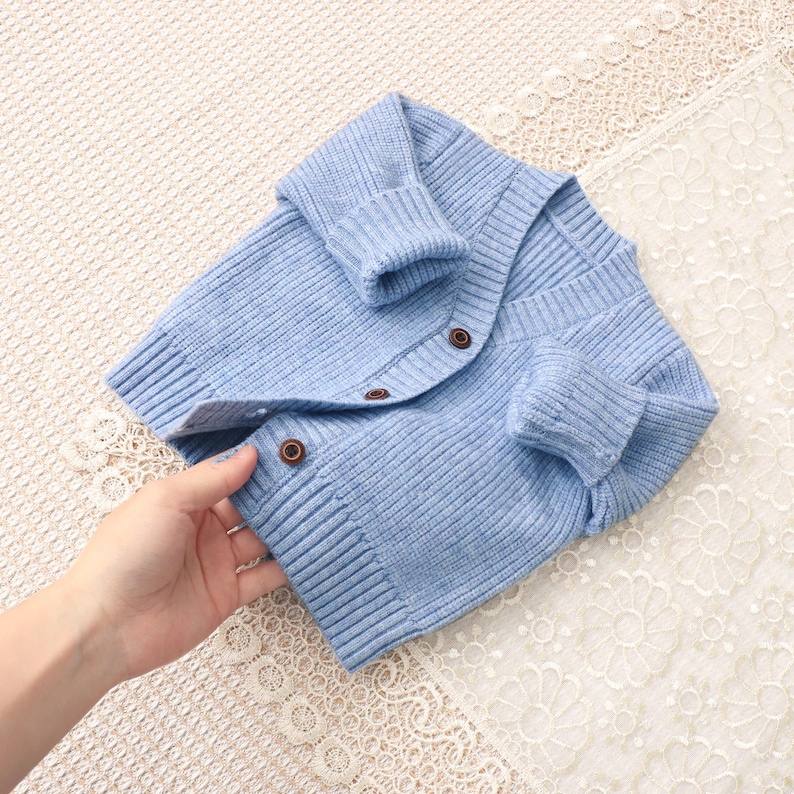 Peut inclure: Un cardigan en tricot bleu clair avec des poignets et un ourlet c&ocirc;tel&eacute;s. Le cardigan a un col en V et se ferme avec trois boutons marron. Le v&ecirc;tement est fait d'une mati&egrave;re douce et textur&eacute;e.