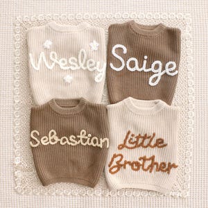May include: Four knitted sweaters in beige and brown, each with embroidered text. The names "Wesley", "Saige", and "Sebastian" are in white or beige, while "Little Brother" is in brown. The sweaters are on a lace background.