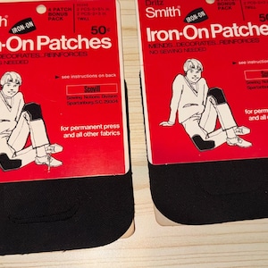 May include: Two packages of Dritz Smith iron-on patches. Each package has a red background with black patches and a drawing of a person. The text on the package reads "Iron-On Patches" and "Mends, Decorates, Reinforces, No Sewing Needed."