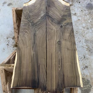 May include: Two pieces of dark brown wood with a natural edge and a unique grain pattern. The wood is likely walnut and has been cut into slabs for woodworking projects.