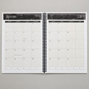 May include: A spiral-bound monthly planner open to January, featuring a black and white landscape header, a grid layout with numbered days, and the Blue Sky logo. The calendar includes marked dates for Epiphany and Martin Luther King Jr. Day.
