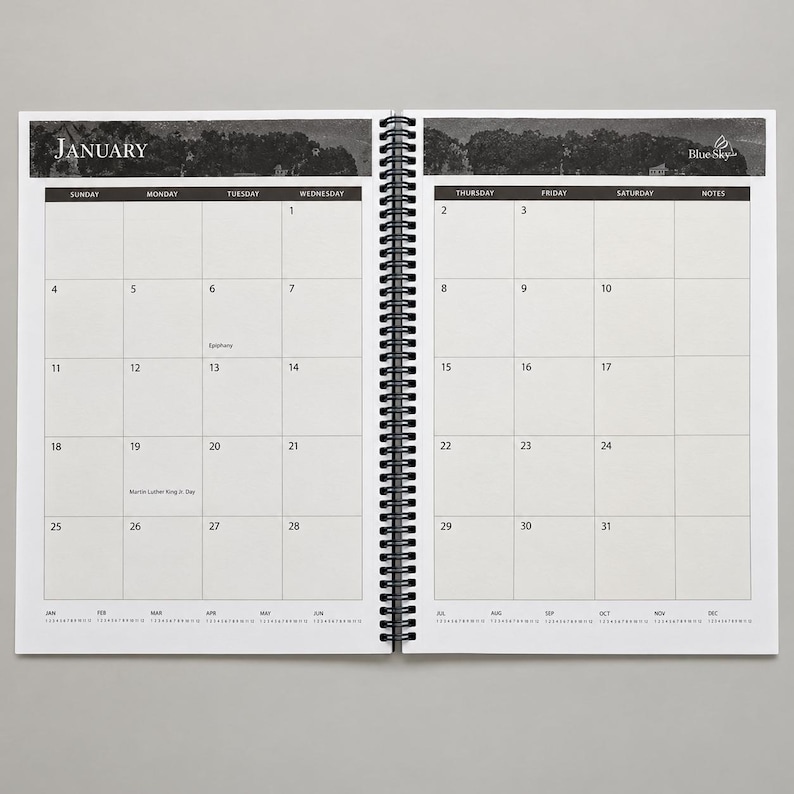 May include: A spiral-bound monthly planner open to January, featuring a black and white landscape header, a grid layout with numbered days, and the Blue Sky logo. The calendar includes marked dates for Epiphany and Martin Luther King Jr. Day.