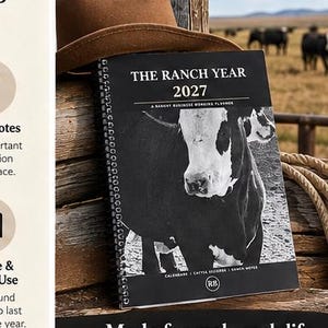 May include: A spiral-bound planner titled The Ranch Year 2027, A Ranch Business Working Planner, featuring a black and white photograph of a cow on the cover, resting against a brown felt hat and stacked wooden logs.