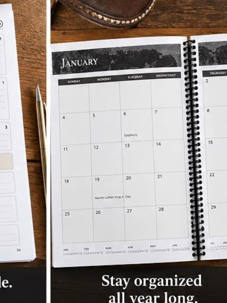 May include: A spiral-bound planner open to a January calendar page with black and white headers, grid lines, and text including Epiphany and Martin Luther King Jr. Day. A gold pen rests beside the planner on a wooden surface.