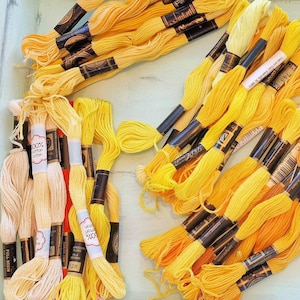 May include: A collection of yellow embroidery floss skeins, neatly arranged in a light blue tray. The floss varies in shades of yellow, from pale to vibrant, with black and white labels. The image includes the text "CRAFT supplies by Jane".