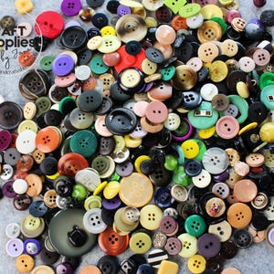 May include: A selection of multi-coloured buttons in different sizes and shapes. The buttons are in shades of red, green, yellow, black, white, and brown. The image includes the text "CRAFT supplies by Jana, handmade-handcrafted-dedicated".