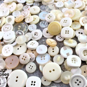 Peut inclure: Un assortiment de boutons blanc cassé et crème de différentes formes et tailles. Les boutons sont ronds, carrés et plats, avec deux ou quatre trous. L'image contient le texte "Craft Supplies by Jane".