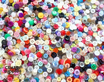 Puede incluir: Una colección de botones coloridos de varios tamaños y formas. Los botones son de tonos rojos, azules, verdes, amarillos, morados y blancos. Algunos botones tienen dos agujeros, otros cuatro. La imagen incluye el texto "Craft Supplies Jana".