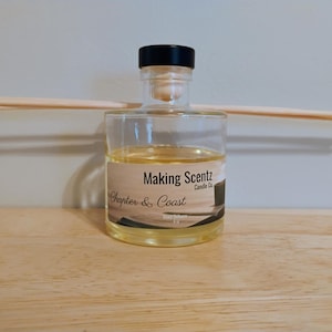 May include: A clear glass diffuser bottle with a black cap and wooden reeds. The bottle contains a yellow liquid and a label that reads "Making Scentz Chapter & Coast Candle Co."