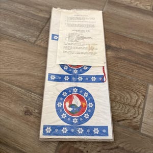May include: A package of holiday can covers with a white background. The covers feature a blue and red circular design with a goose and snowflakes. The package also includes a recipe for Chocolate Cherry Bites.