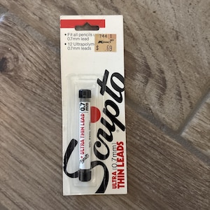 May include: A package of Scripto Ultra Thin Lead 0.7mm leads. The white and red package has the Scripto logo in black. The package includes a tube of 0.7mm leads and text that says "Fit all pencils" and "12 Ultrapolym 0.7mm leads."