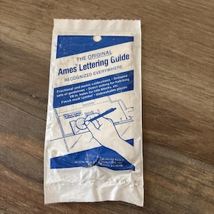 Puede incluir: Guía de rotulación Ames en un paquete de plástico blanco y azul. El paquete presenta el texto "THE ORIGINAL Ames Lettering Guide" e incluye detalles sobre calibraciones fraccionarias y métricas, y orificios de 3,18 mm.