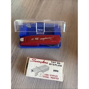 May include: A red Swingline Tot 50 stapler in a blue base with a clear plastic cover. Below is a small box of Swingline Tot 50 staples. The box is white with red and black text. The staples are chisel pointed.