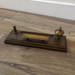 Peut inclure: Un organisateur de bureau rectangulaire en bois avec une finition brun foncé, comprenant un porte-stylo en laiton, un plateau central en laiton pour petits objets et un encrier en laiton avec couvercle. La base présente des bords biseautés.