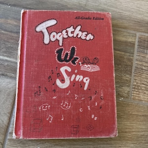 May include: A vintage red book titled "Together We Sing" with white and black lettering. The cover features musical notes and illustrations. The book is an "All-Grades Edition" and shows signs of wear.
