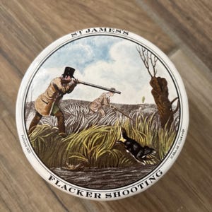 Puede incluir: Plato decorativo redondo y blanco con una escena de caza. La ilustración muestra a dos hombres con rifles, un perro y el texto "ST JAMES'S" y "FLACKER SHOOTING". Publicado en 1820.