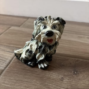 May include: A ceramic dog figurine with a black nose, white fur, and black and white accents. The dog has a red heart-shaped tongue and is sitting on a wooden surface. The figurine is a decorative item.