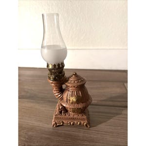 May include: A decorative miniature oil lamp with a clear glass chimney and a frosted globe. The lamp has a brown base with gold accents and ornate detailing. The lamp is approximately 6 inches tall.