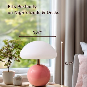 May include: A compact and elegant table lamp with a pink spherical base and a white mushroom-shaped shade. The lamp is 8.7 inches tall, 7.9 inches wide, and 4.7 inches deep. Text on the image reads "Compact & Elegant" and "Fits Perfectly on Nightstands & Desks."