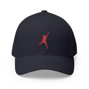 May include: Navy blue baseball cap with a red silhouette of a person jumping. The cap has a curved brim and a structured fit. The embroidered logo is on the front of the cap.