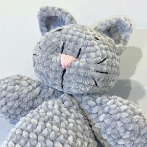 Puede incluir: Un juguete de peluche gris hecho a mano con forma de gato, con una nariz rosa y bigotes negros. El gato tiene orejas grandes y redondeadas y est&aacute; hecho de un material suave y texturizado. El juguete est&aacute; dise&ntilde;ado para ser tierno y es adecuado para ni&ntilde;os.