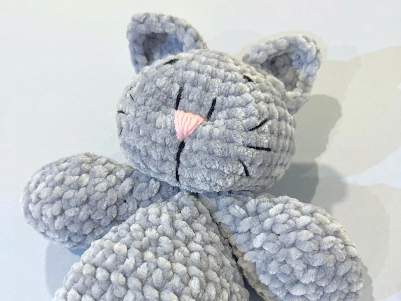 Puede incluir: Un juguete de peluche gris hecho a mano con forma de gato, con una nariz rosa y bigotes negros. El gato tiene orejas grandes y redondeadas y est&aacute; hecho de un material suave y texturizado. El juguete est&aacute; dise&ntilde;ado para ser tierno y es adecuado para ni&ntilde;os.