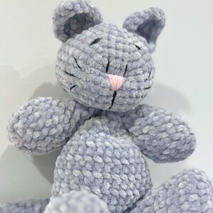 Puede incluir: Un peluche de gato gris hecho a mano con ganchillo, con una nariz rosa y detalles cosidos en negro. El gato tiene orejas grandes y est&aacute; hecho de hilo suave y texturizado. Un animal de peluche lindo y tierno.