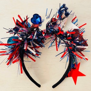 May include: A red, white, and blue headband with a star, heart, and other festive decorations. The headband is made of black elastic and is perfect for a patriotic celebration.