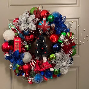 May include: A Christmas wreath decorated with red, green, blue, and silver ornaments, including a miniature red telephone booth, a small Christmas tree, and a silver star. The wreath also features a red, white, and blue patterned ornament with the word "London" on it.