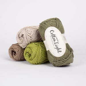 May include: A collection of yarn balls in various colors, including beige, brown, green, and olive green. One ball has a label that reads "Cotton Light". The yarn is arranged in a pile, suggesting a craft or knitting project.