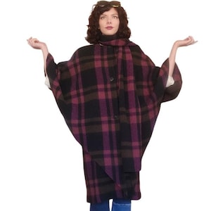 May include: A woman wearing a plaid cape in shades of black, burgundy, and brown. The cape has a matching scarf and is buttoned in the front. She is wearing blue patchwork jeans and brown shoes.
