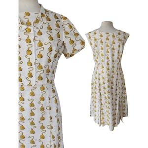 May include: Two white dresses with a repeating gold-colored pocket watch pattern. One dress has short sleeves and a collared neckline, while the other is sleeveless with a round neckline. Both dresses are knee-length.