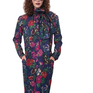 May include: A long-sleeved knee-length dress in a dark blue fabric featuring a vibrant floral pattern of red, pink, and purple roses with green leaves. The dress includes a high neckline with a large integrated bow tie and two side pockets.