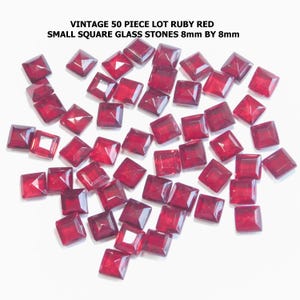 May include: A collection of fifty vintage ruby red square glass stones, each measuring 8mm by 8mm. The stones are scattered across a white surface, showcasing their faceted design and deep red color. The text "VINTAGE 50 PIECE LOT RUBY RED SMALL SQUARE GLASS STONES 8mm BY 8mm" is visible.