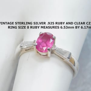 May include: Vintage sterling silver ring with a .925 ruby and clear CZ stone. The ring size is 8. The ruby measures 6.53mm by 6.17mm. The ring is displayed on a white surface.
