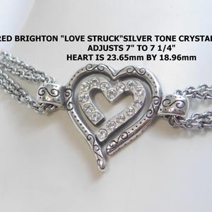 May include: A silver-tone crystal heart bracelet with a double chain design. The heart-shaped pendant is adorned with clear crystals and measures approximately 0.93 inches by 0.75 inches. The bracelet adjusts from 7 to 7 1/4 inches. Text on the image reads: RETIRED BRIGHTON "LOVE STRUCK" SILVER TONE CRYSTAL HEART BRACELET ADJUSTS 7" TO 7 1/4" HEART IS 23.65mm BY 18.96mm