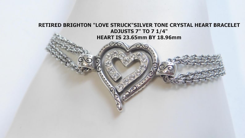 May include: A silver-tone crystal heart bracelet with a double chain design. The heart-shaped pendant is adorned with clear crystals and measures approximately 0.93 inches by 0.75 inches. The bracelet adjusts from 7 to 7 1/4 inches. Text on the image reads: RETIRED BRIGHTON "LOVE STRUCK" SILVER TONE CRYSTAL HEART BRACELET ADJUSTS 7" TO 7 1/4" HEART IS 23.65mm BY 18.96mm