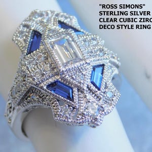 May include: Sterling silver Art Deco style ring with blue and clear cubic zirconia stones. The ring is size 6 and features a detailed design with geometric shapes and sparkling accents. The text "ROSS SIMONS" is visible.