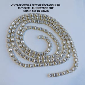 May include: Vintage brass chain set with rectangular cut Czech rhinestones. The chain is over 4 feet long and features clear, sparkling stones set in a gold-toned metal. The text in the image reads: "VINTAGE OVER 4 FEET OF RECTANGULAR CUT CZECH RHINESTONE CUP CHAIN SET IN BRASS."
