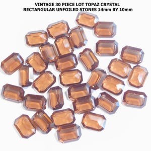 May include: A collection of thirty vintage topaz crystal stones. The rectangular, unfaceted stones are a warm brown color and measure 14mm by 10mm. The text in the image reads "VINTAGE 30 PIECE LOT TOPAZ CRYSTAL RECTANGULAR UNFOILED STONES 14mm BY 10mm."