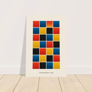 May include: A framed print with a grid of coloured squares in red, blue, yellow, and black. The artwork, titled "Chromatic Balance - 2025," is displayed against a white wall and rests on a wooden floor.