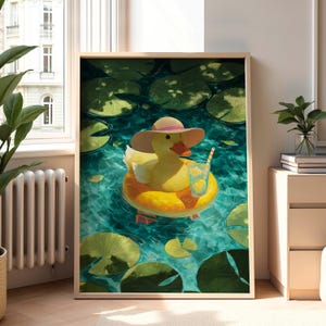 May include: Framed art print featuring a yellow duck wearing a sun hat and floating on a yellow inflatable ring in a pond. The duck is holding a glass of lemonade with a straw. The pond is surrounded by lily pads.