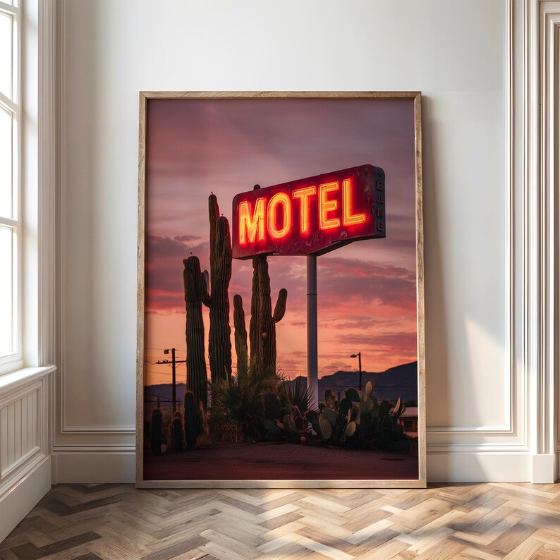 Pode incluir: Impress&atilde;o emoldurada com uma placa de motel vintage com a palavra "MOTEL" em n&eacute;on vermelho brilhante. A placa est&aacute; situada contra um c&eacute;u de p&ocirc;r do sol com cactos em primeiro plano. A imagem evoca uma paisagem des&eacute;rtica.