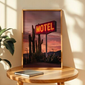 Pode incluir: Uma impress&atilde;o emoldurada com uma placa de motel vintage com a palavra "MOTEL" em n&eacute;on vermelho brilhante contra um c&eacute;u ao p&ocirc;r do sol. Cactos altos e plantas do deserto est&atilde;o em primeiro plano. A impress&atilde;o est&aacute; em uma moldura de madeira.