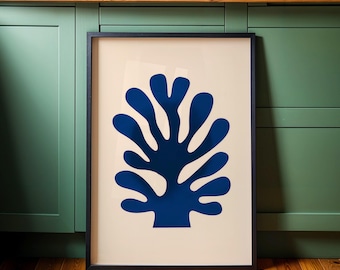 Puede incluir: Una impresión artística enmarcada con un diseño abstracto azul marino que se asemeja a un árbol o coral sobre un fondo crema. La obra de arte está encerrada en un marco negro y descansa contra una pared verde y un suelo de madera.