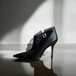 May include: Black leather ankle boots with a pointed toe and a high heel. The boots feature a buckle detail on the side.