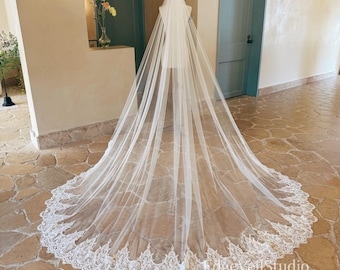 May include: A long, floor-length ivory bridal veil draped over a mannequin. The veil features a sheer, lightweight tulle fabric with an intricate, scalloped white lace trim along the entire bottom edge. The text EdgeVeilStudio is visible.