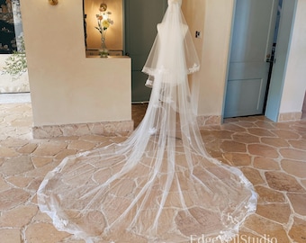 May include: A long, white, sheer tulle wedding veil draped over a mannequin. The veil features delicate white floral lace appliqués along the edges and scattered across the train. The text EdgeveilStudio is visible in the bottom right corner.