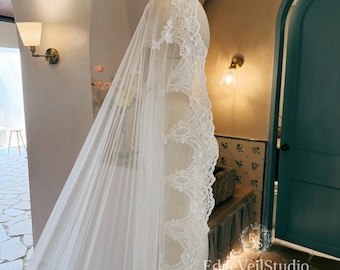 May include: A long white wedding veil draped over a mannequin, featuring intricate floral lace trim along the edges. The sheer tulle fabric extends downward, and the text EdgeVeilStudio is visible in the lower right corner of the image.