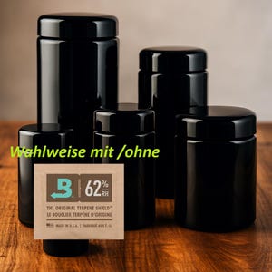 Pode incluir: Uma coleção de potes pretos brilhantes com tampas de vários tamanhos. Um pequeno pacote retangular com o texto "THE ORIGINAL TERPENE SHIELD" e "62% RH" está em frente aos potes. O texto "Wahlweise mit /ohne" também é visível.